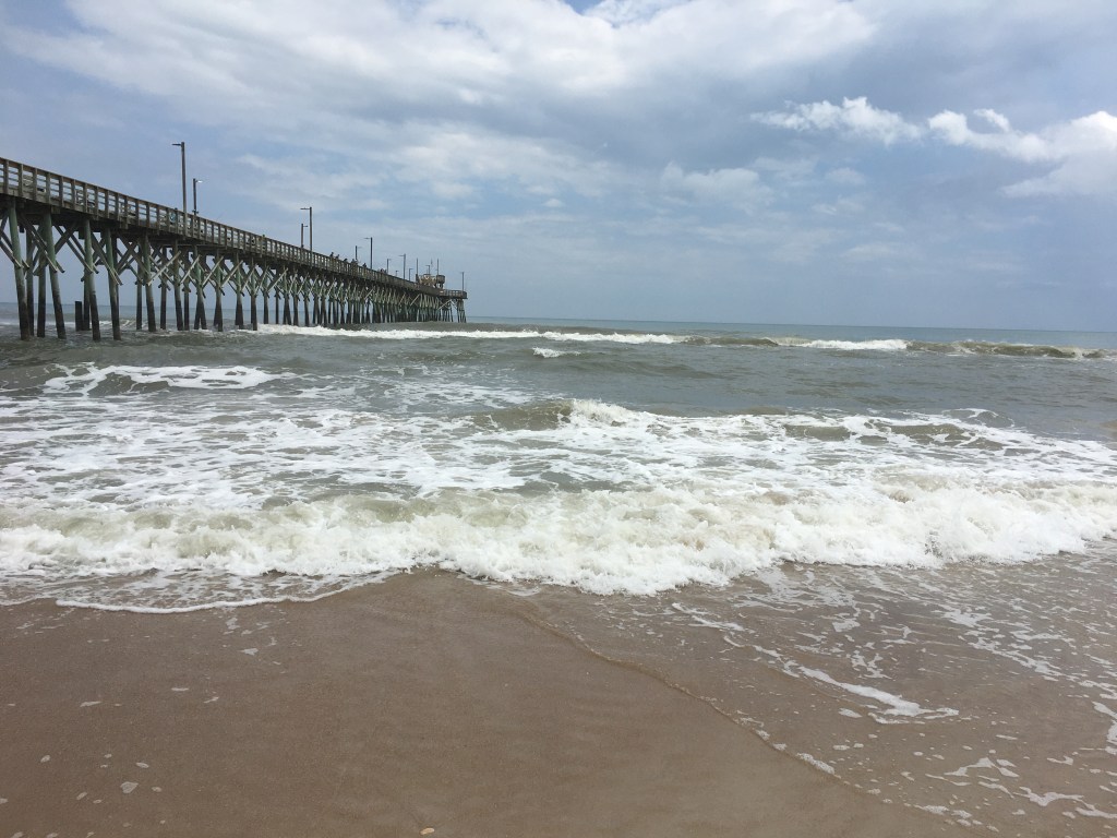 Ocean waves of blue and green, white foam, and a fishing pier.